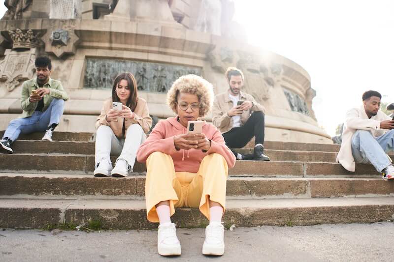 Eine Gruppe junger Menschen sitzt auf einer Treppe, alle schauen auf ihr Smartphone.