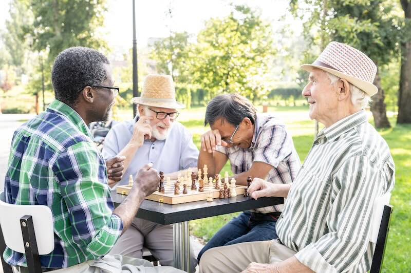 Eine Gruppe älterer Männer sitzt in einem Park und spielt Schach.