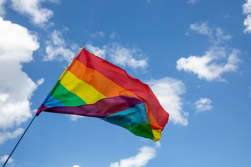 Ein Regenbogenfahne vor blauem Himmel.